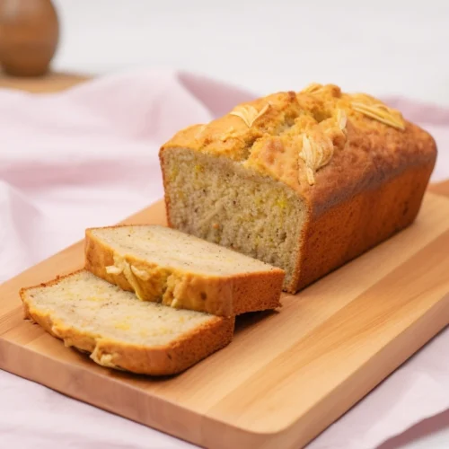 The Easiest Banana Bread Recipe You’ll Ever Make! 2 A beautifully plated classic Simply Recipes Banana Bread loaf with a golden brown crust and a soft, fluffy yellow interior. The bread is placed on a wooden cutting board, with two slices neatly arranged beside it. A blush pink linen napkin and a pastel green background create a warm, inviting feel.