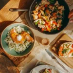 Family-friendly international lunch inspirations spread featuring salmon nigiri, chicken fajitas, philly cheesesteak tortellini, and special sandwich with small travel decorations on rustic wooden table